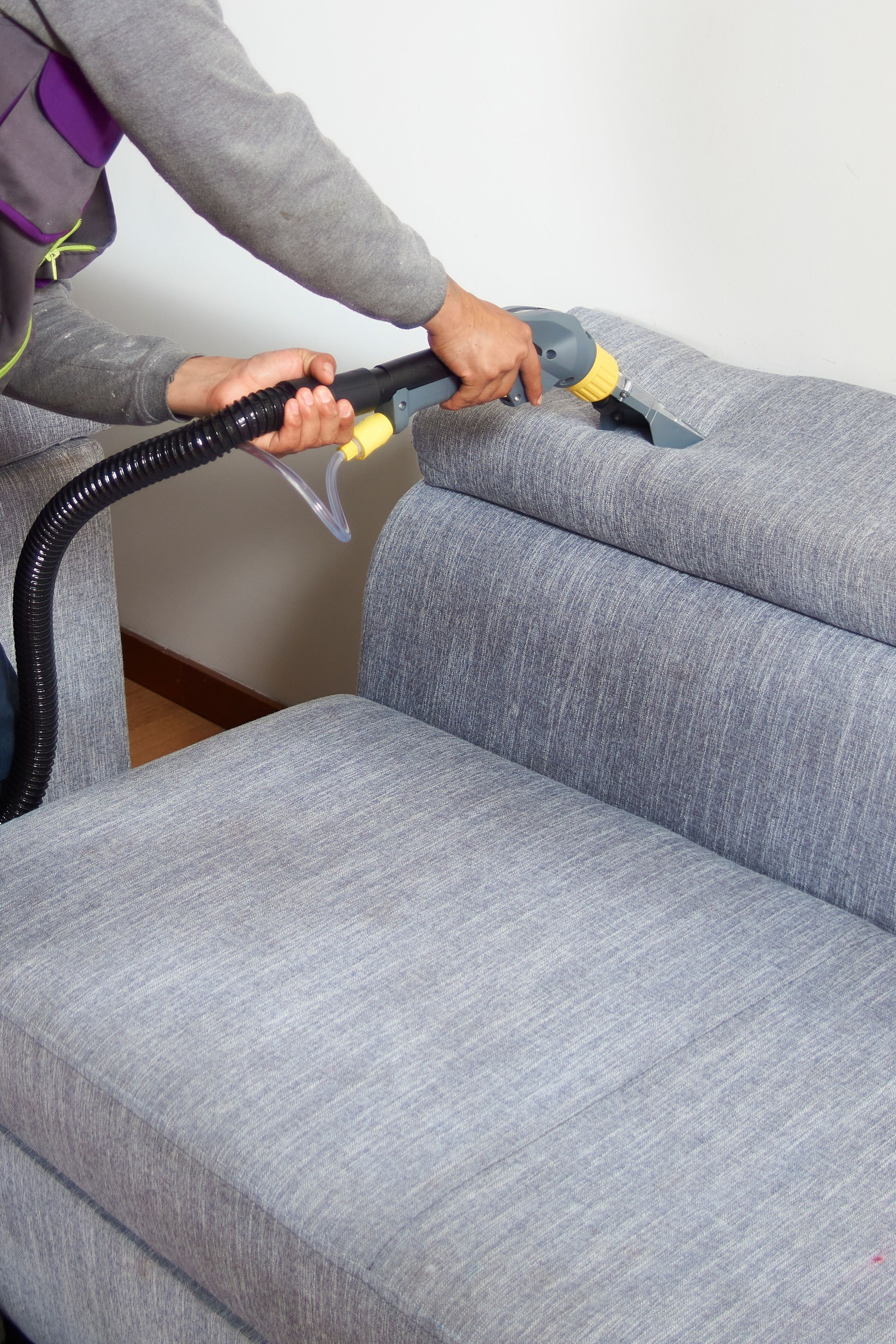 vertical shot of A man is cleaning a cough with a steam cleaner.